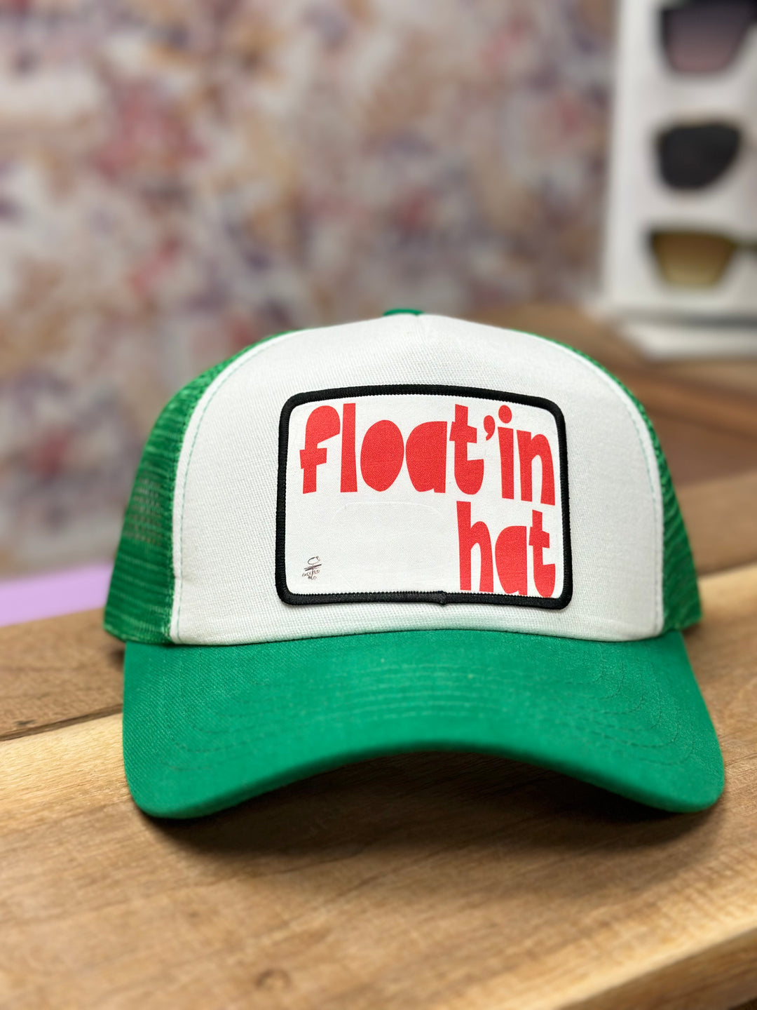 A green and white trucker hat with 'FLOAT'IN' text on the front.