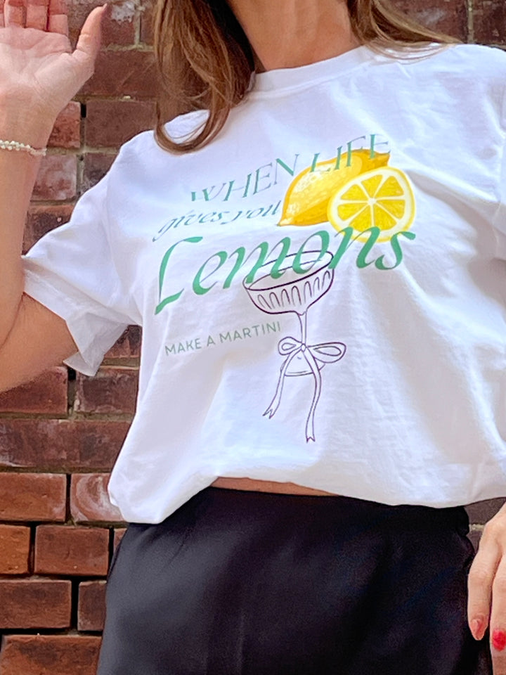 Person wearing a white t-shirt with a lemon-themed design against a brick wall.