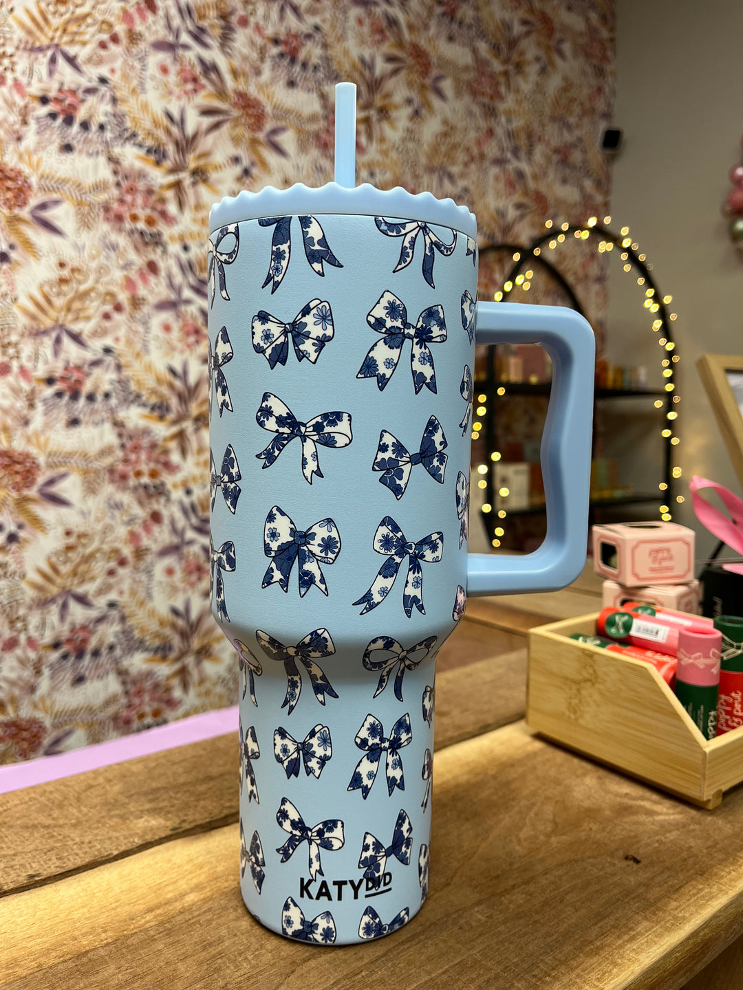 A light blue stainless steel tumbler with a pattern of white and blue bows, featuring a screw-on plastic top and an easy-to-hold handle.