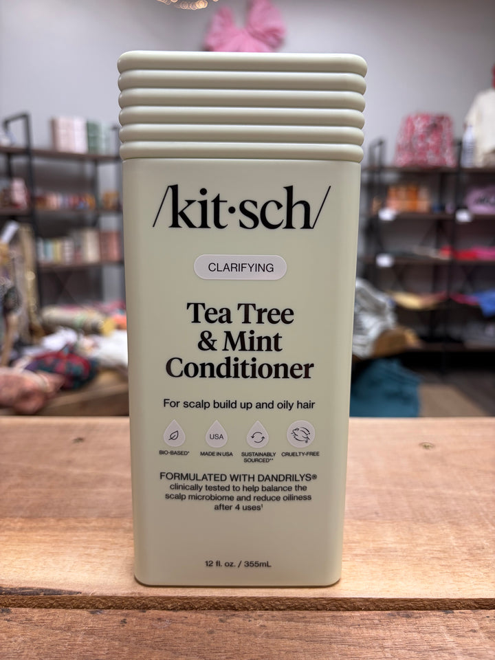 Kitsch Tea Tree & Mint Conditioner bottle on a wooden surface with blurred background