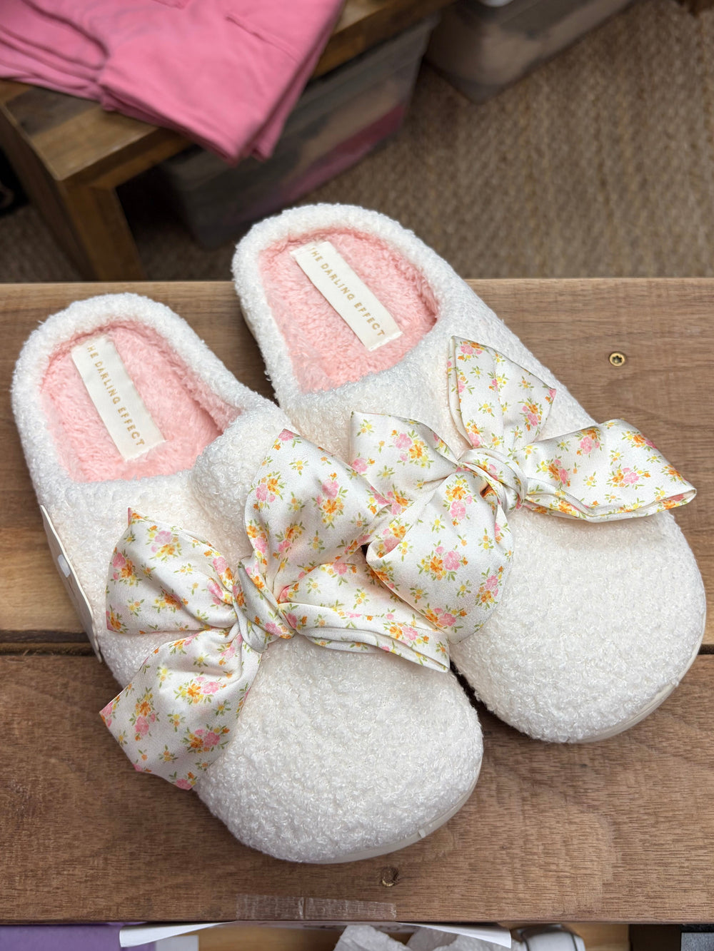 Pair of white slippers with floral bows on a wooden surface