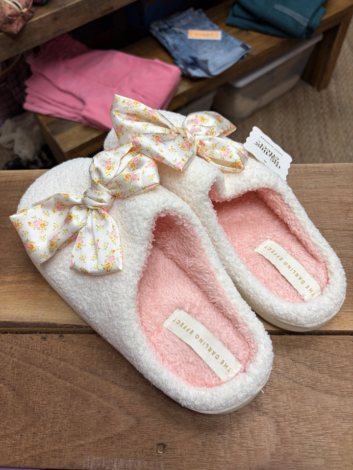 Pair of pink slippers with floral bows on a wooden surface