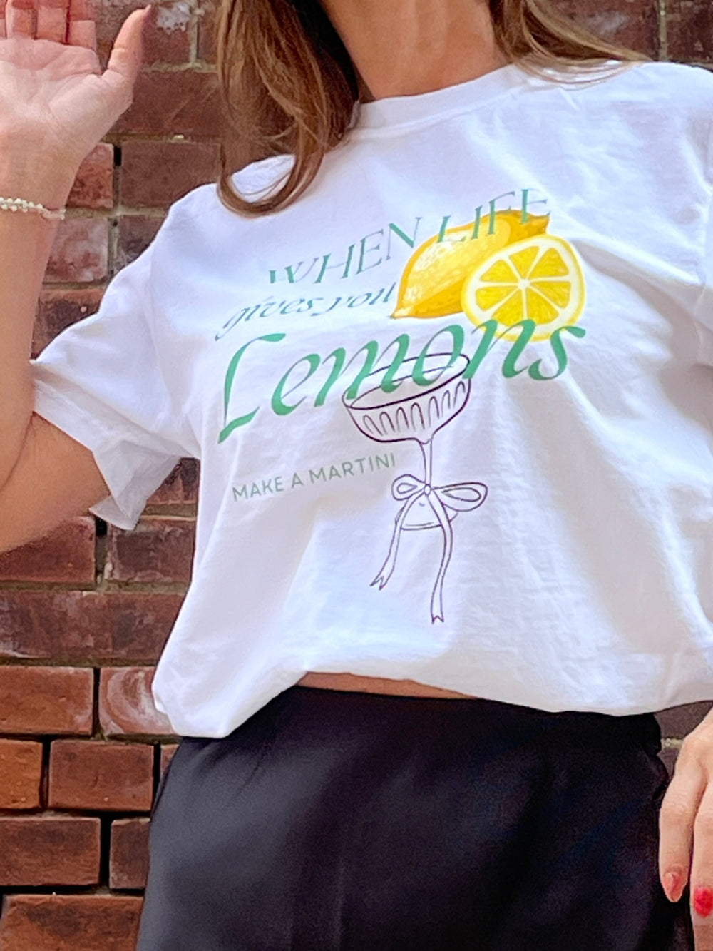 Person wearing a white t-shirt with a lemon-themed design against a brick wall.