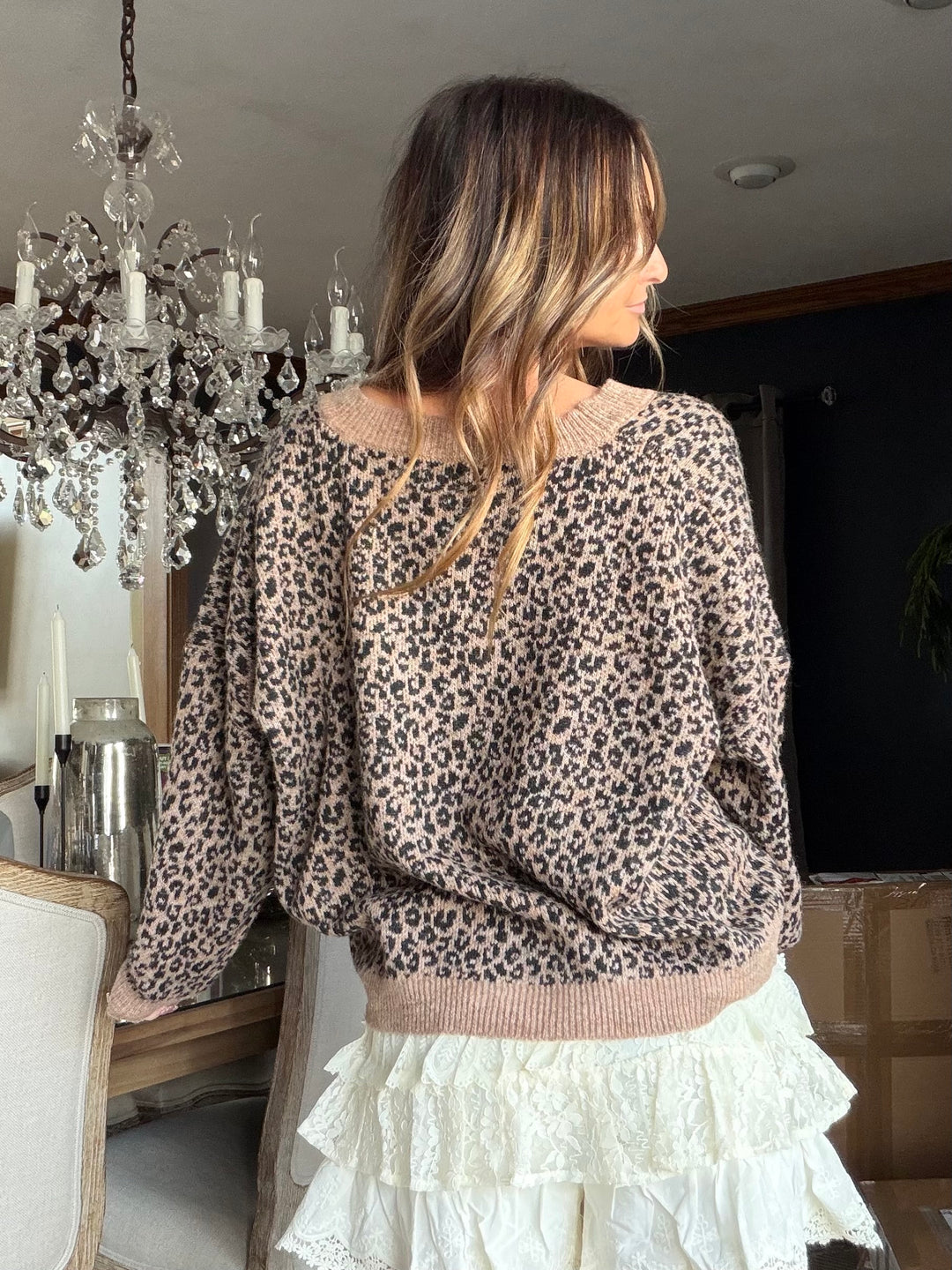 Woman wearing a leopard print sweater and white skirt in a room with a chandelier.