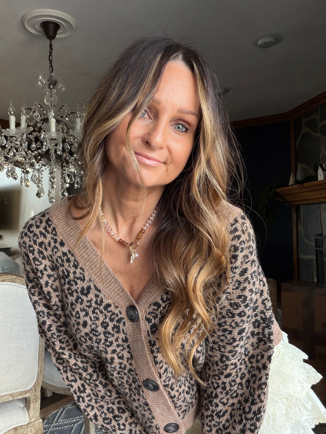 Woman wearing a leopard print cardigan in an indoor setting with a chandelier.