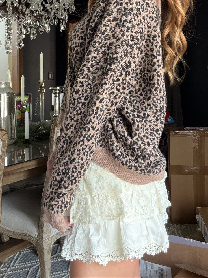 Woman wearing a leopard print sweater and white skirt in a room with a chandelier.