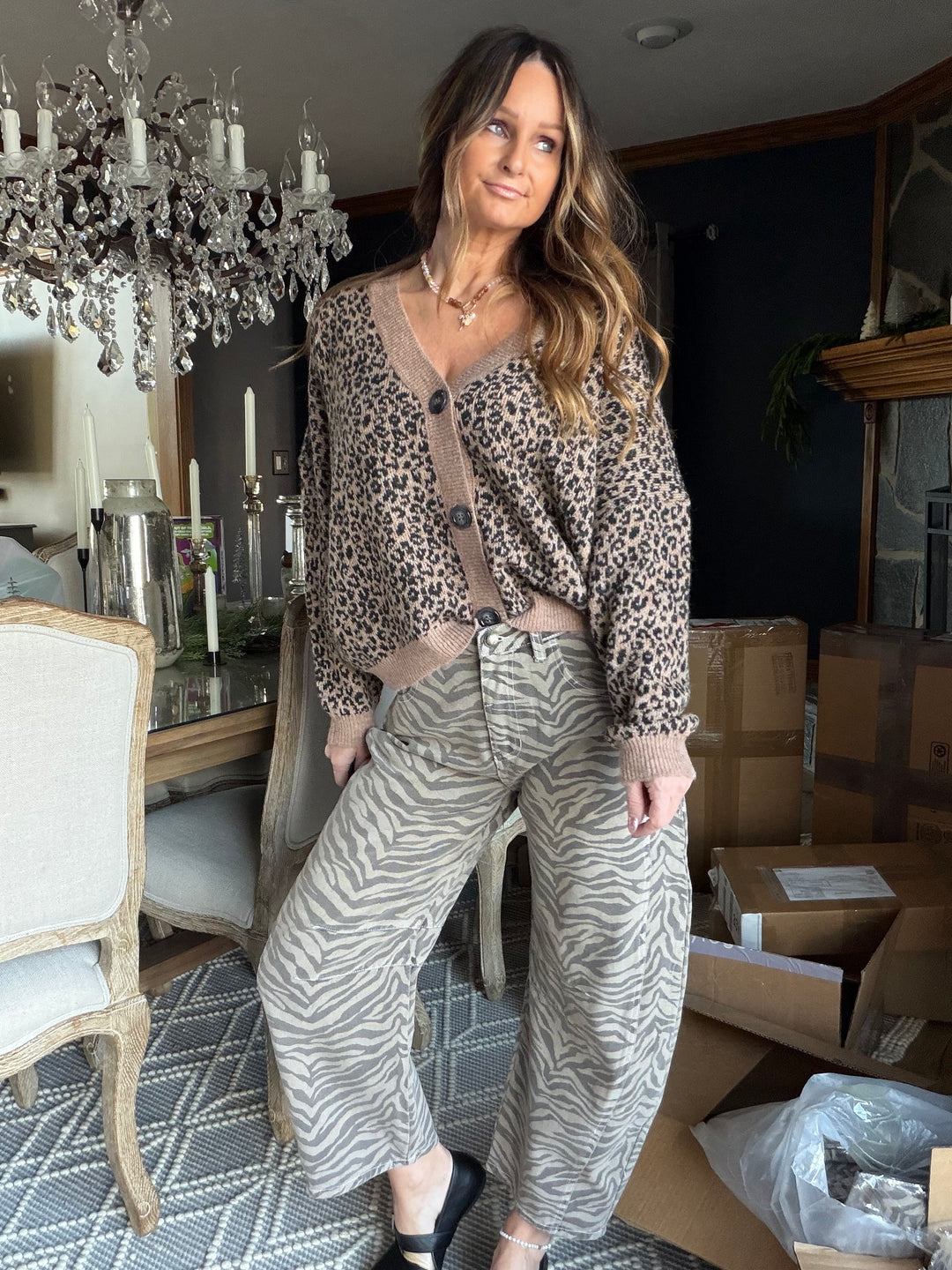 Woman in leopard print top and zebra pattern pants standing in a room with boxes and decor.