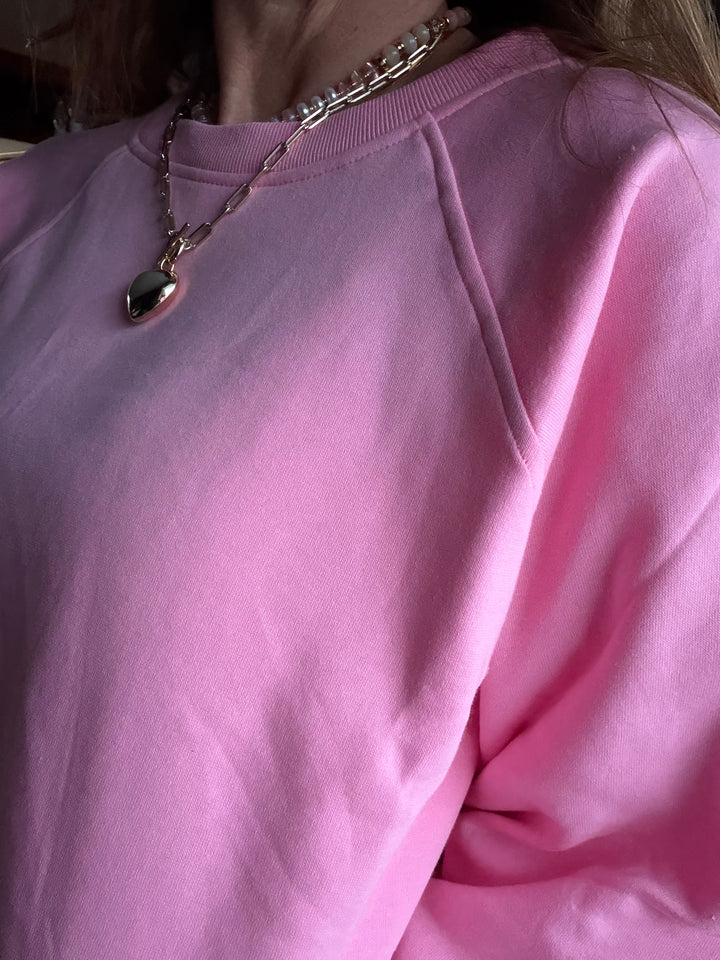 Close-up of a pink sweatshirt with a necklace featuring a heart-shaped pendant.
