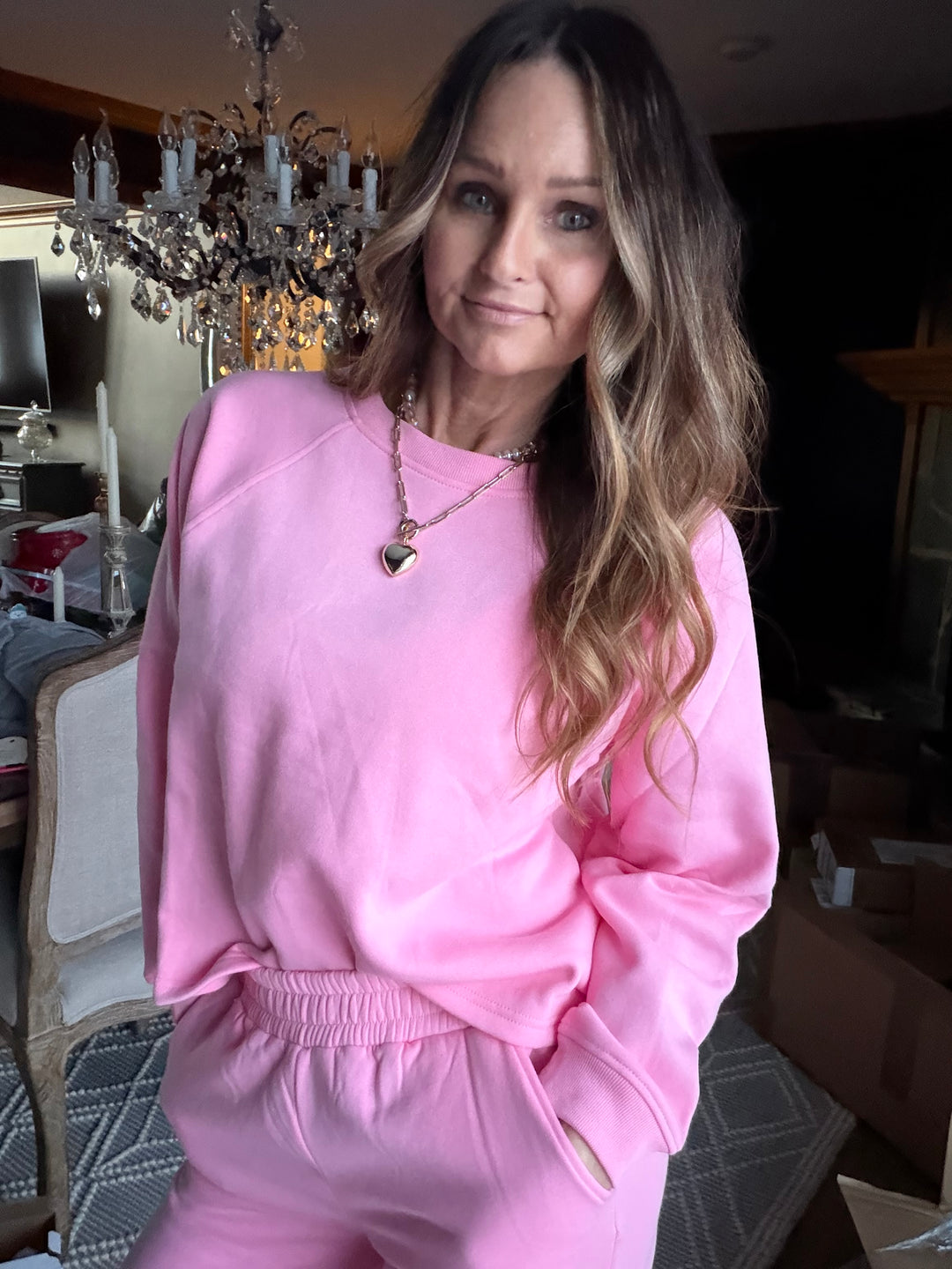 Woman wearing a pink outfit in an indoor setting with a chandelier in the background.