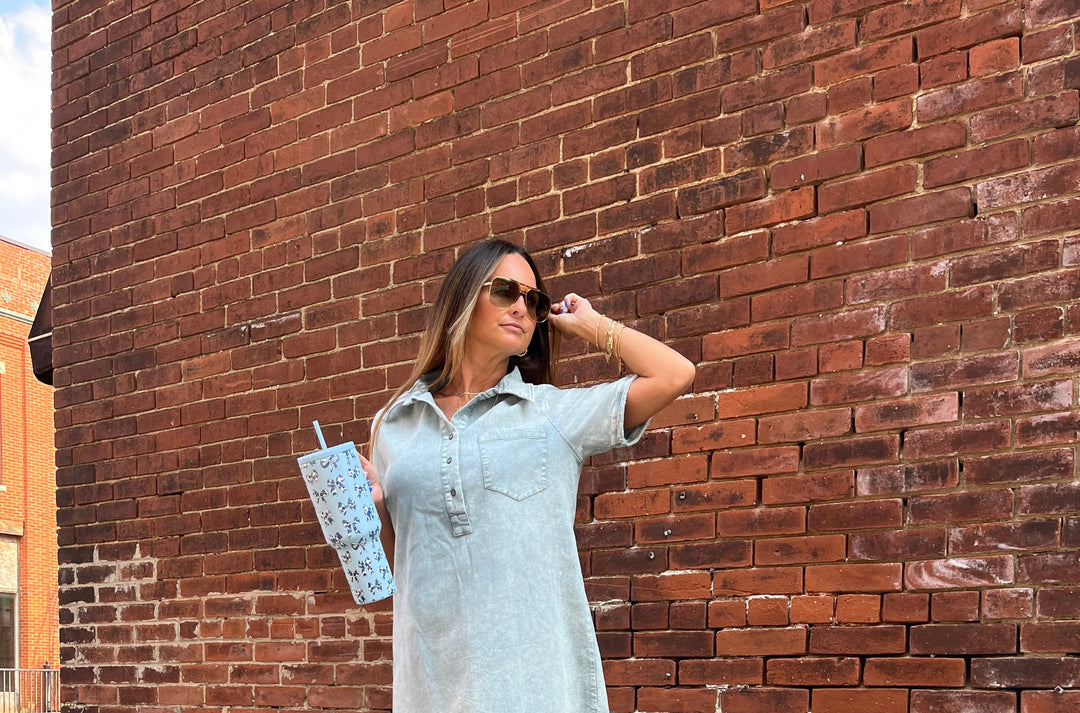 Woman in a light-colored dress standing against a brick wall.