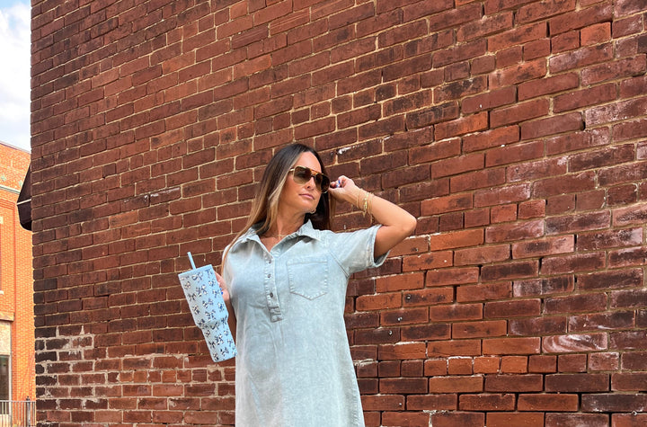 Woman in a light-colored dress standing against a brick wall.