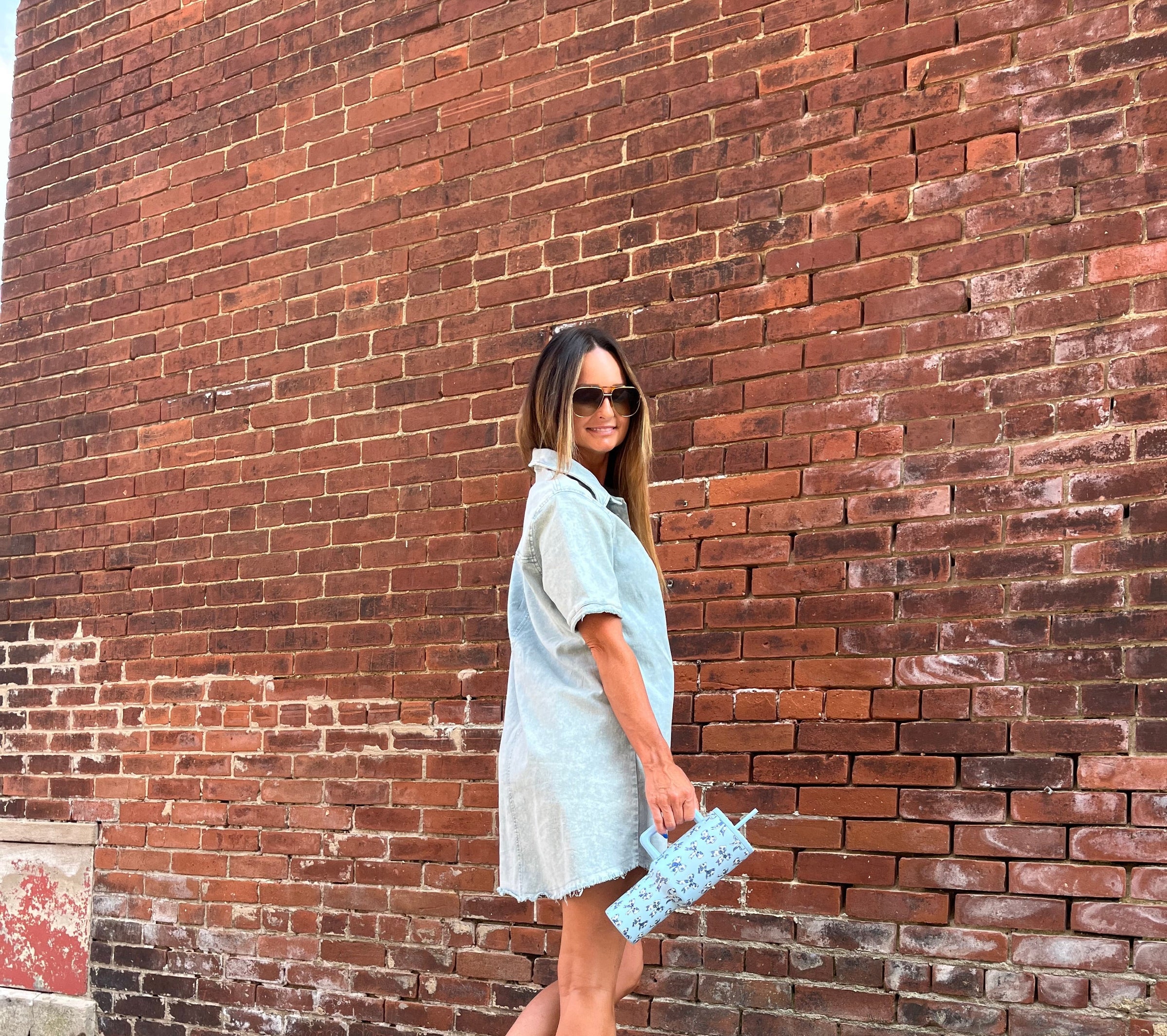 Woman wearing a chambray dress against a brick wall